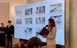 Kobieta na tle tablicy z finalistami konkursu Lider Dostępności w kategorii Mały obiekt użyteczności publicznej