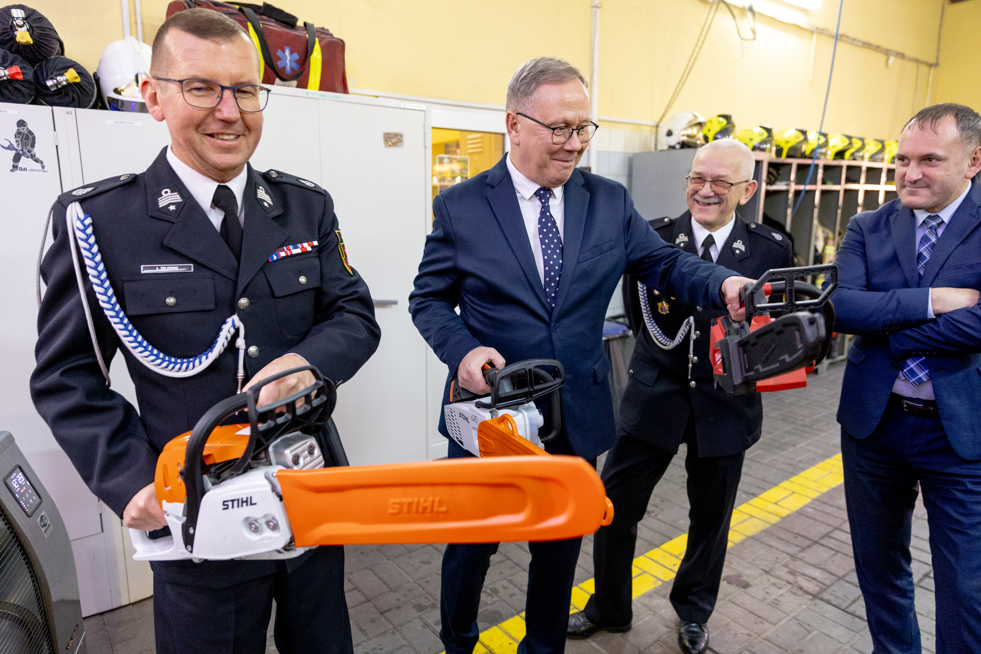 mężczyzna w&nbsp;mundurze strażaka trzyma piłę i&nbsp;mężczyzna w&nbsp;garniturze tez trzyma piłę 