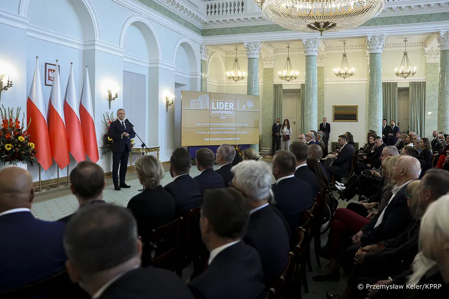 Mężczyzna w&nbsp;Garniturze przemawia do grona ludzi
