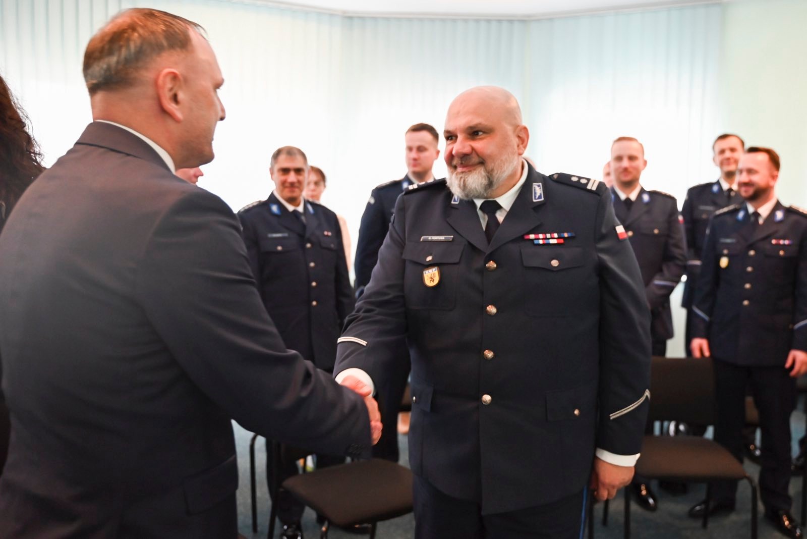 Mężczyzna tyłem składa gratulacje mężczyźnie w&nbsp;mundurze. 