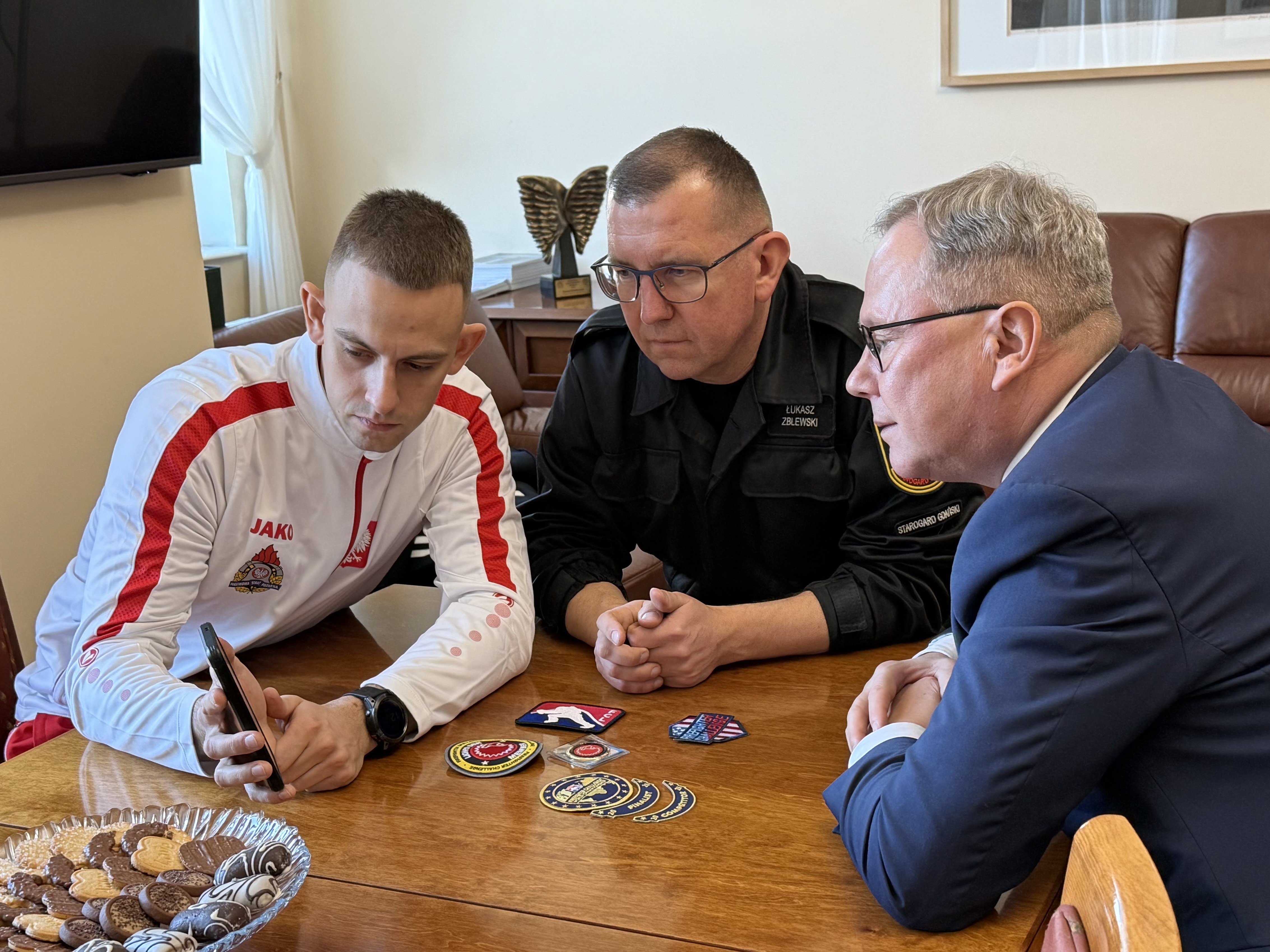 3 mężczyzn przy stole ogląda zdjęcia z&nbsp;zawod&oacute;w.