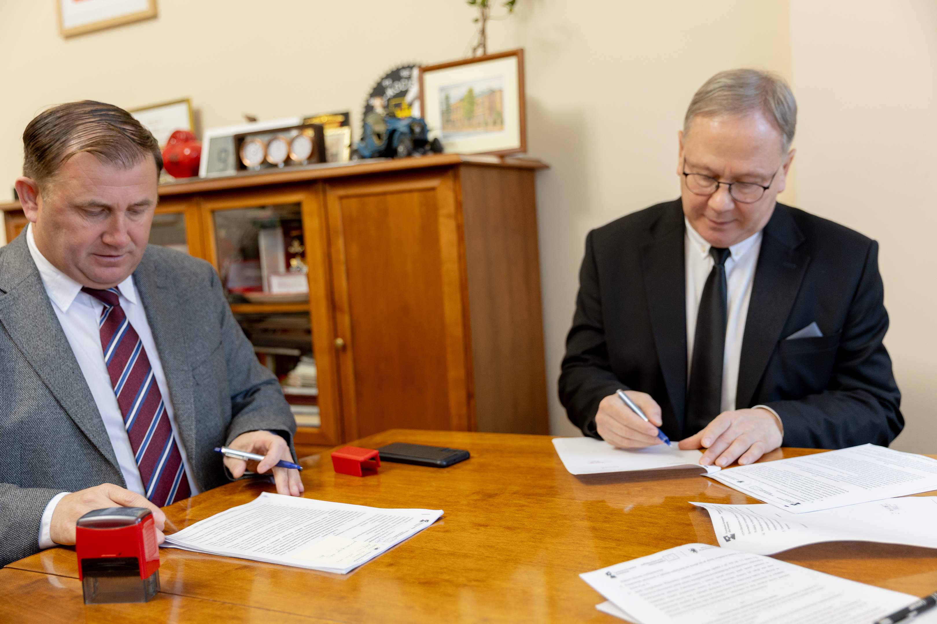 dw&oacute;ch mężczyzn siedzi przy stole  podpisuje dokumenty