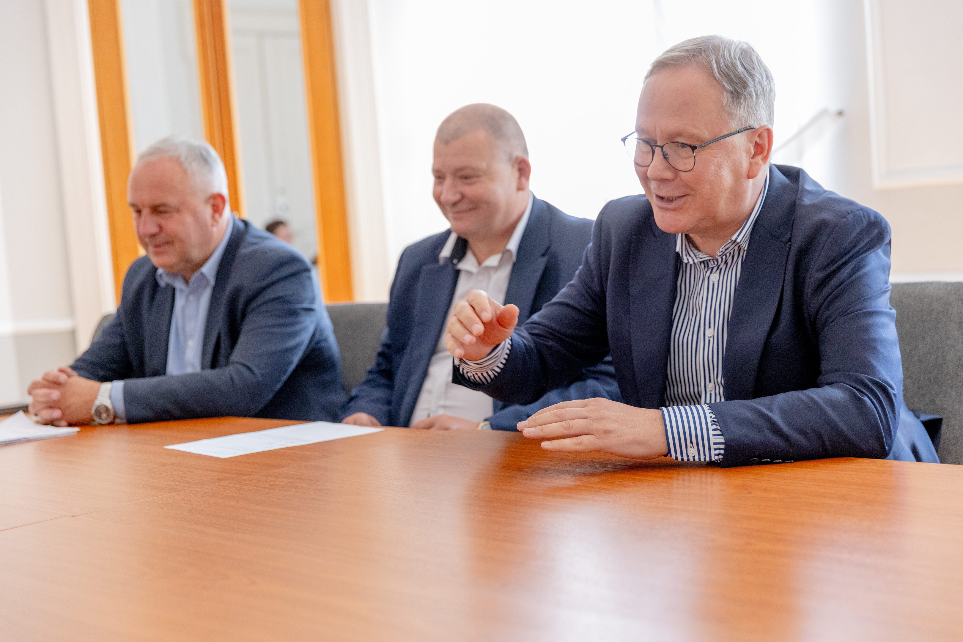 trzech mężczyzn w&nbsp;garniturach przy stole 