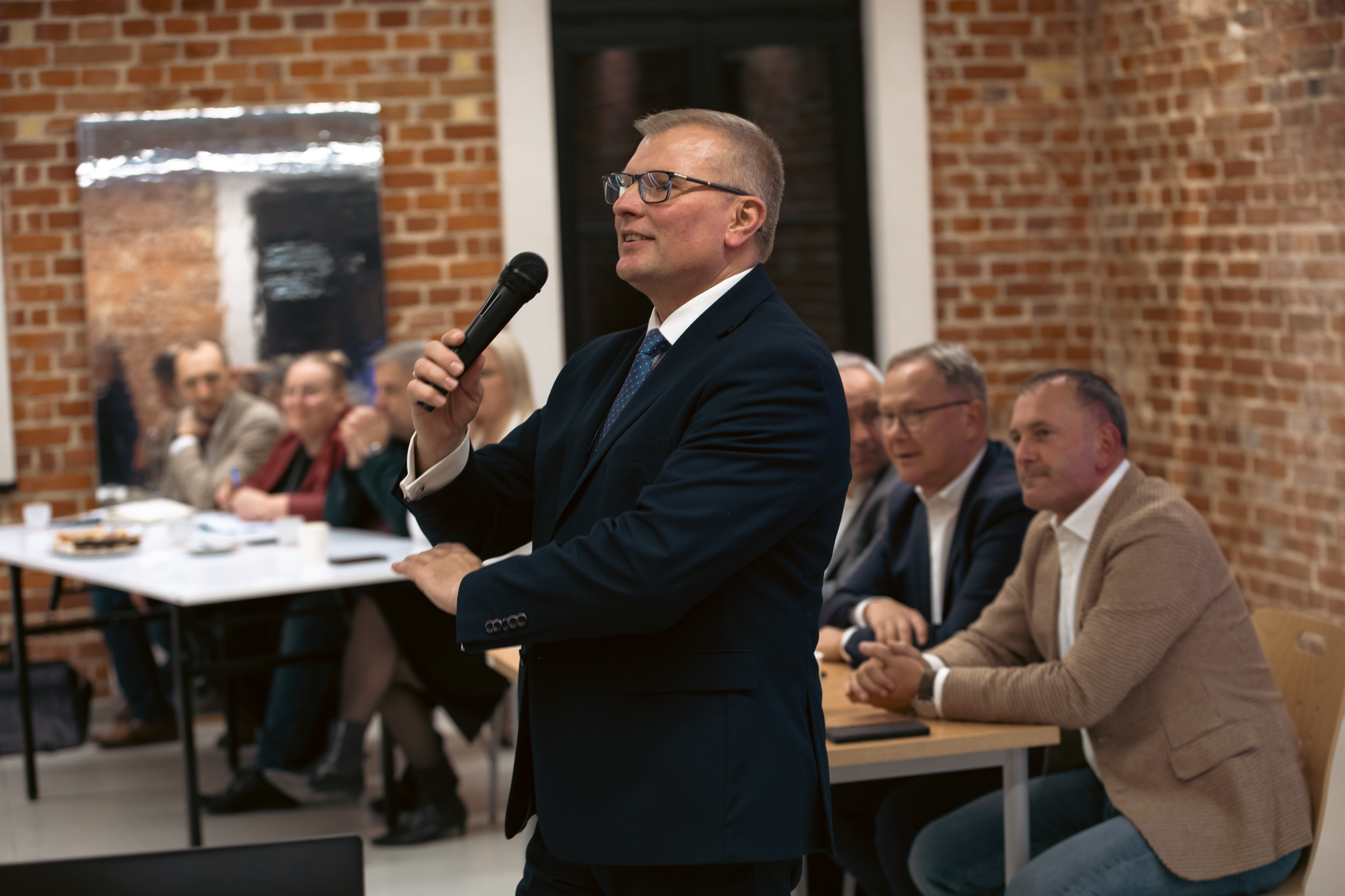Mężczyzna stoi posr&oacute;d siedziących ludzi