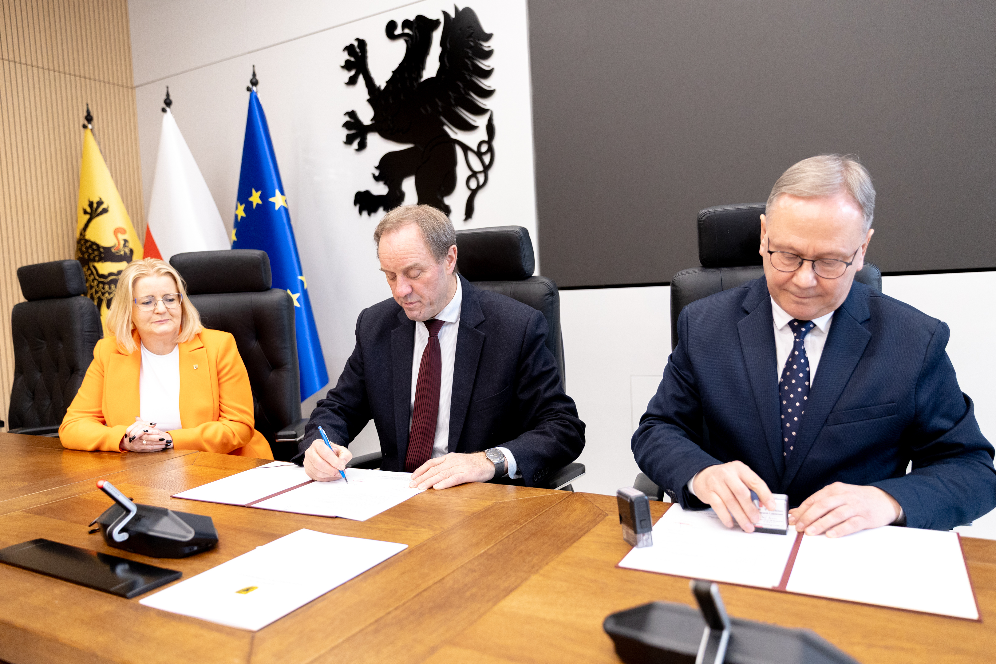 kobie4ta i&nbsp;dw&oacute;ch męzczyzn w&nbsp;garniturach przy stole podpisują dokumenty