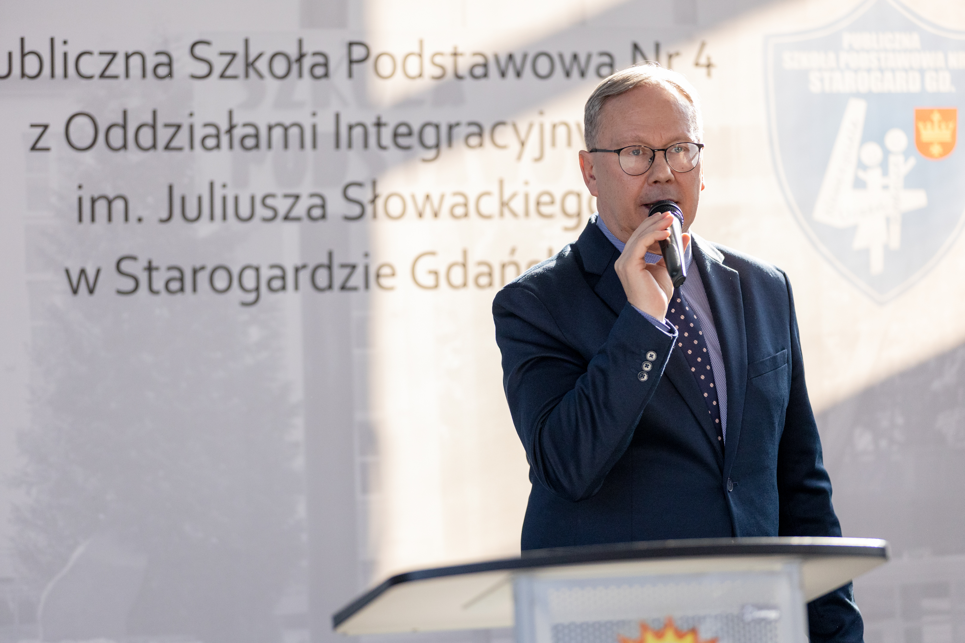 Mężczyna w&nbsp;garniturze przy m&oacute;wnicy z&nbsp;mikrofonem w&nbsp;ręku