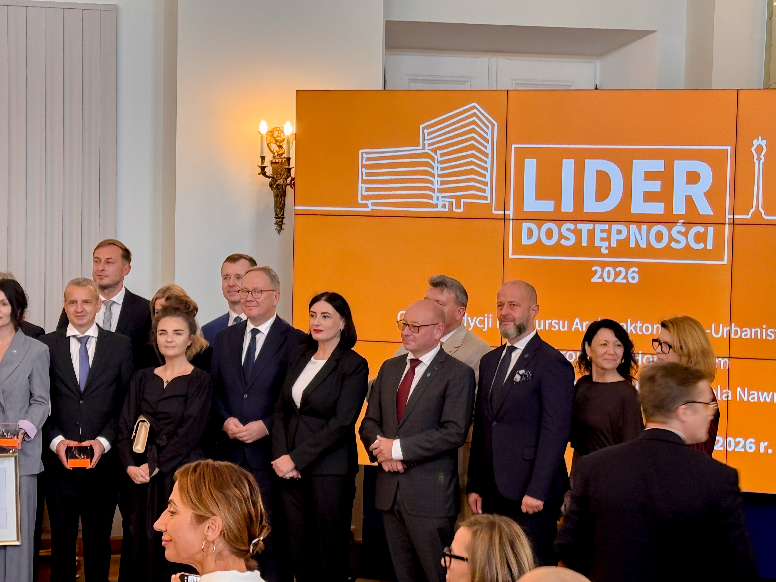 Ludzie na&nbsp;tle tablicy z&nbsp;logo Lider Dostępności