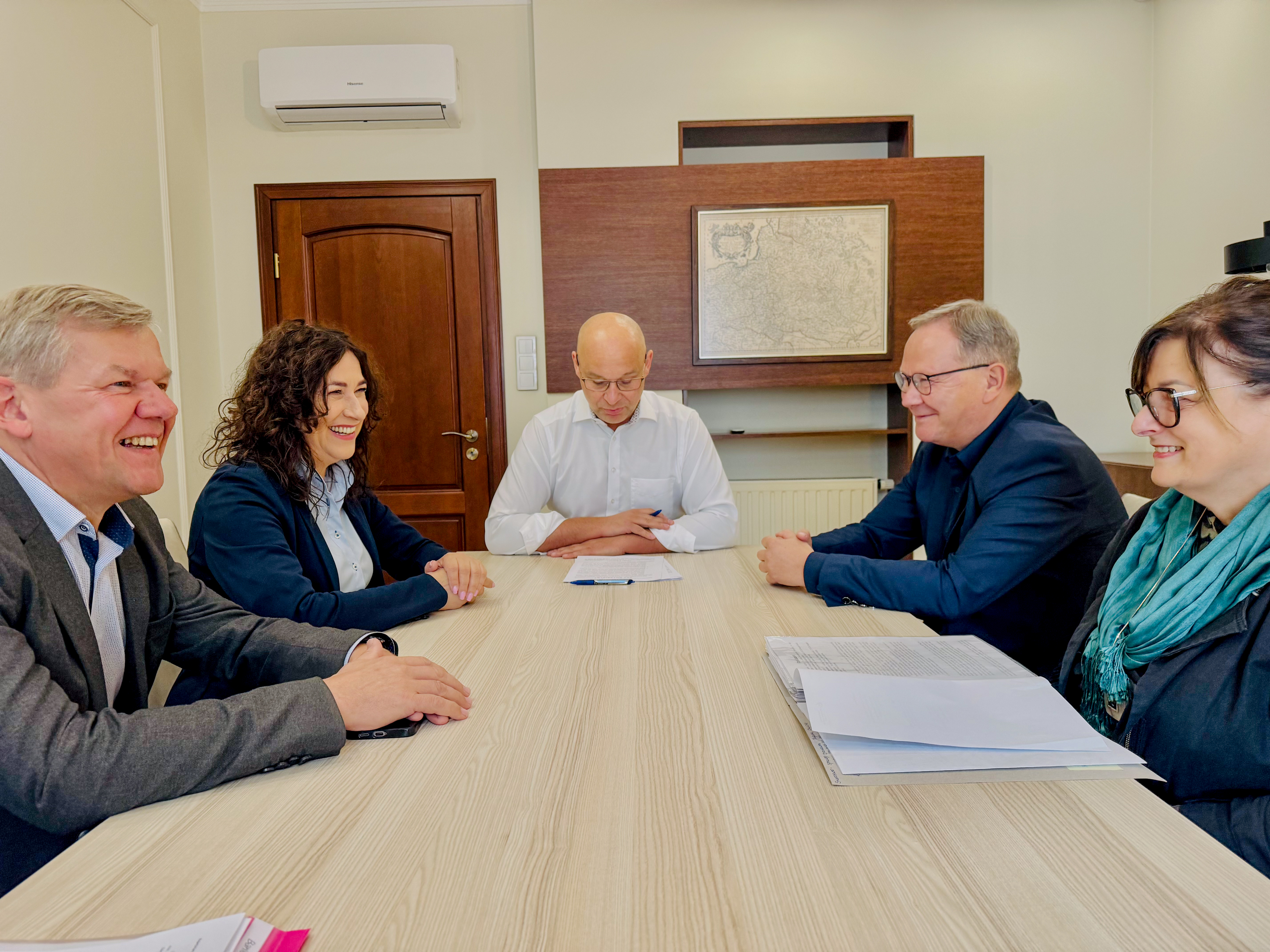 Trzch męzczyzn i&nbsp;dwie kobiety siedza przy stole. Mężczyzna na&nbsp;czele stołu czyta dokumenty