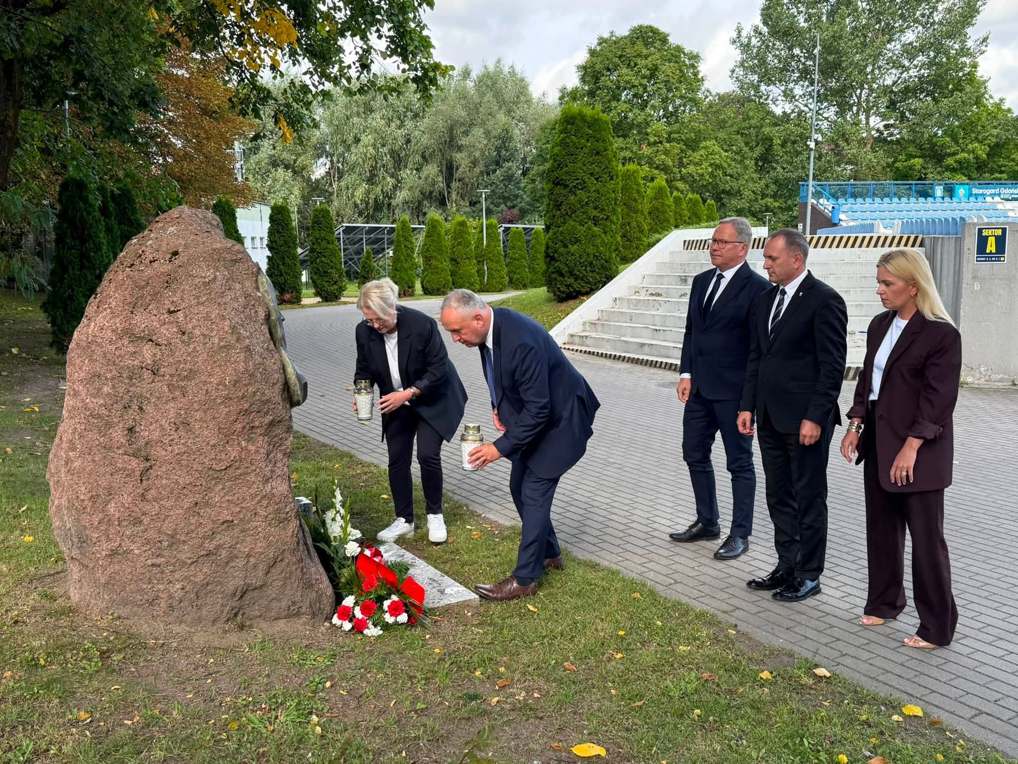 3 mężczyzn i&nbsp;2 kobiety skłądaja kwiaty pod pomnikiem.