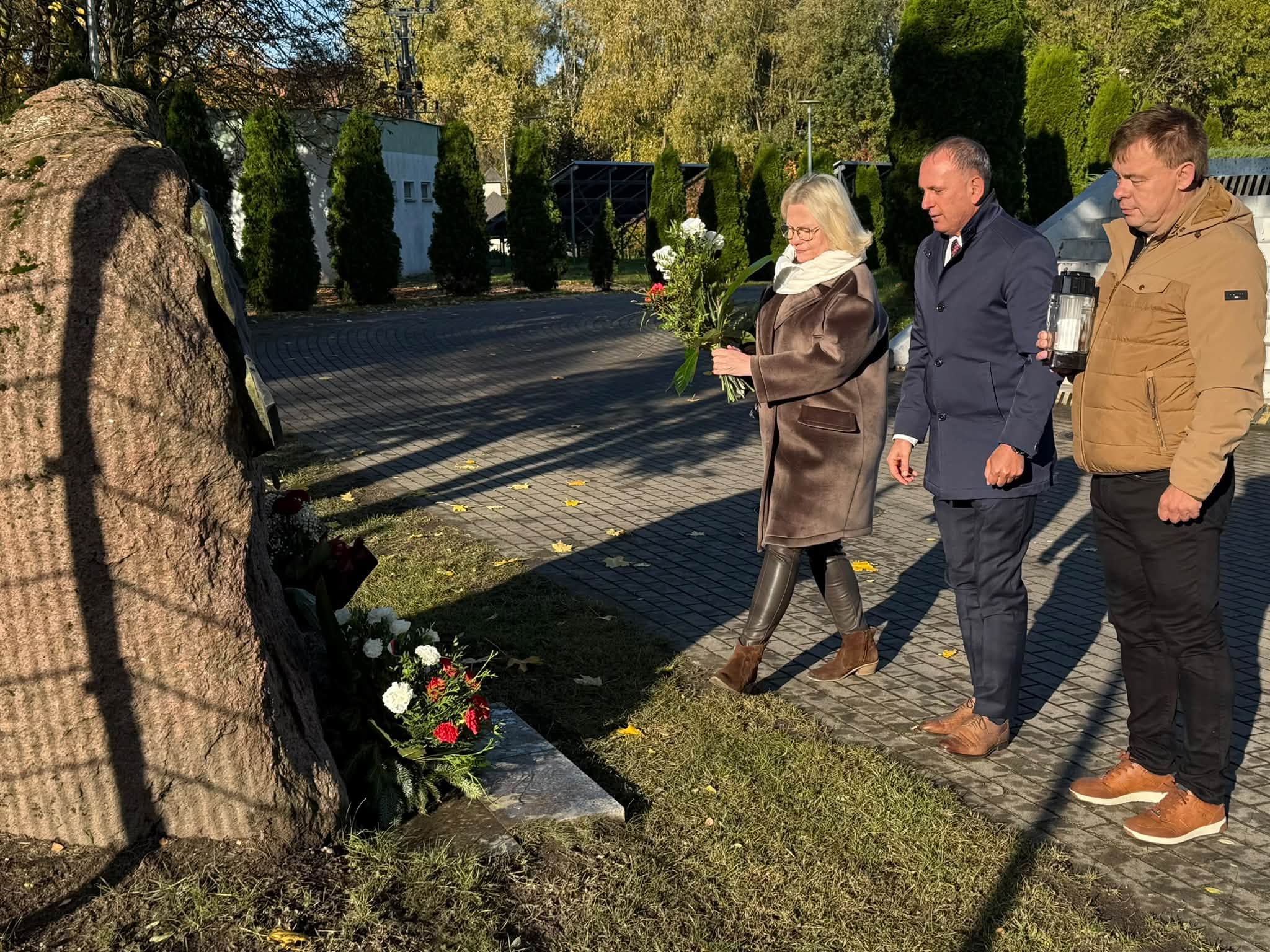 Trzy osoby składaja kwiaty.