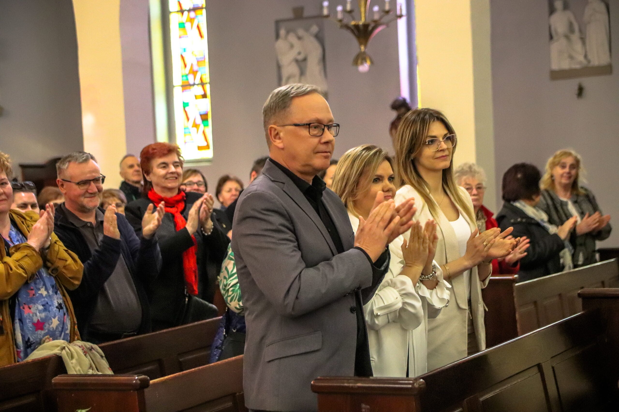 W ławkach stoją ludzie i oklaskują artystystów. Na pierwszym planie męczyzna - prezydent i dwie kobiety - przwodniczące Rady Miasta i Komisji Kultury