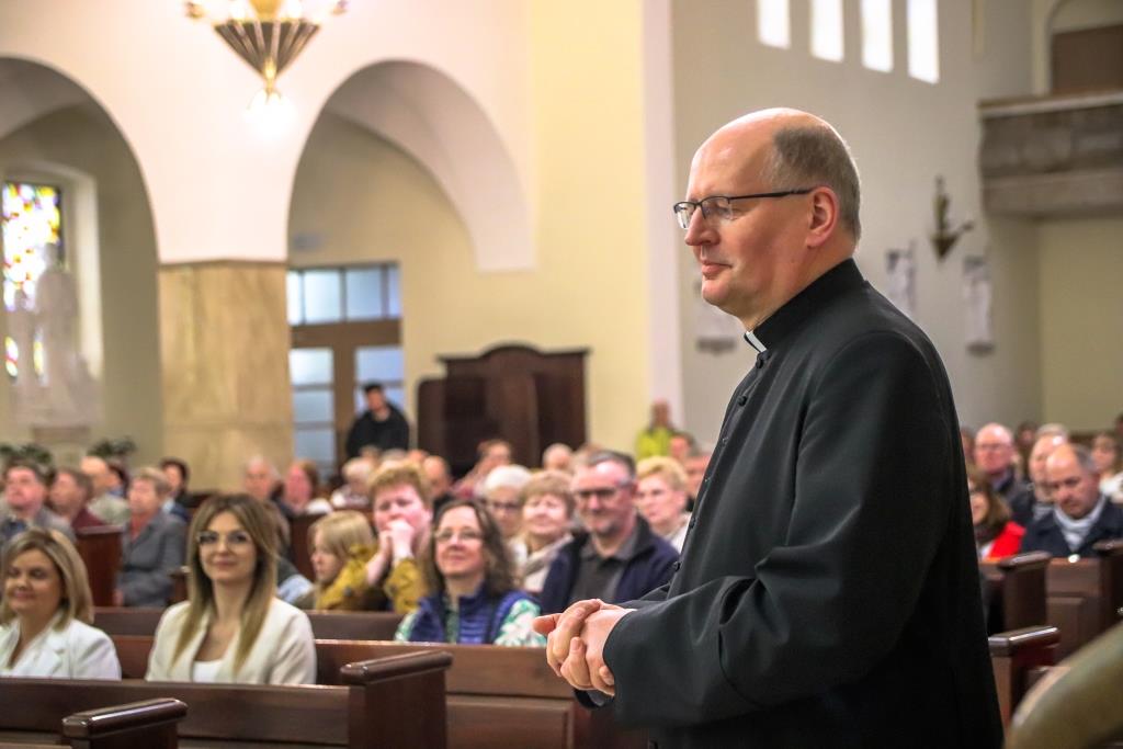 Na pierwszym planie ksiądz w sułtannie za nim w ławkach siedza ludzie