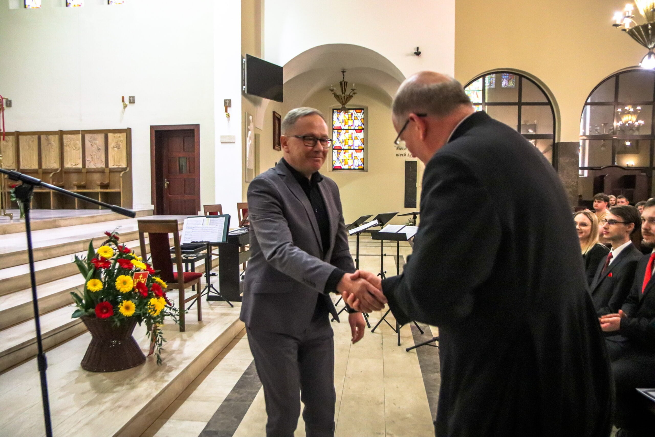 Meżczyzna w garniturze ( prezydnet) sćiska dłoń drugiemu mężczyżnie ( ksiądz w sułtannie)