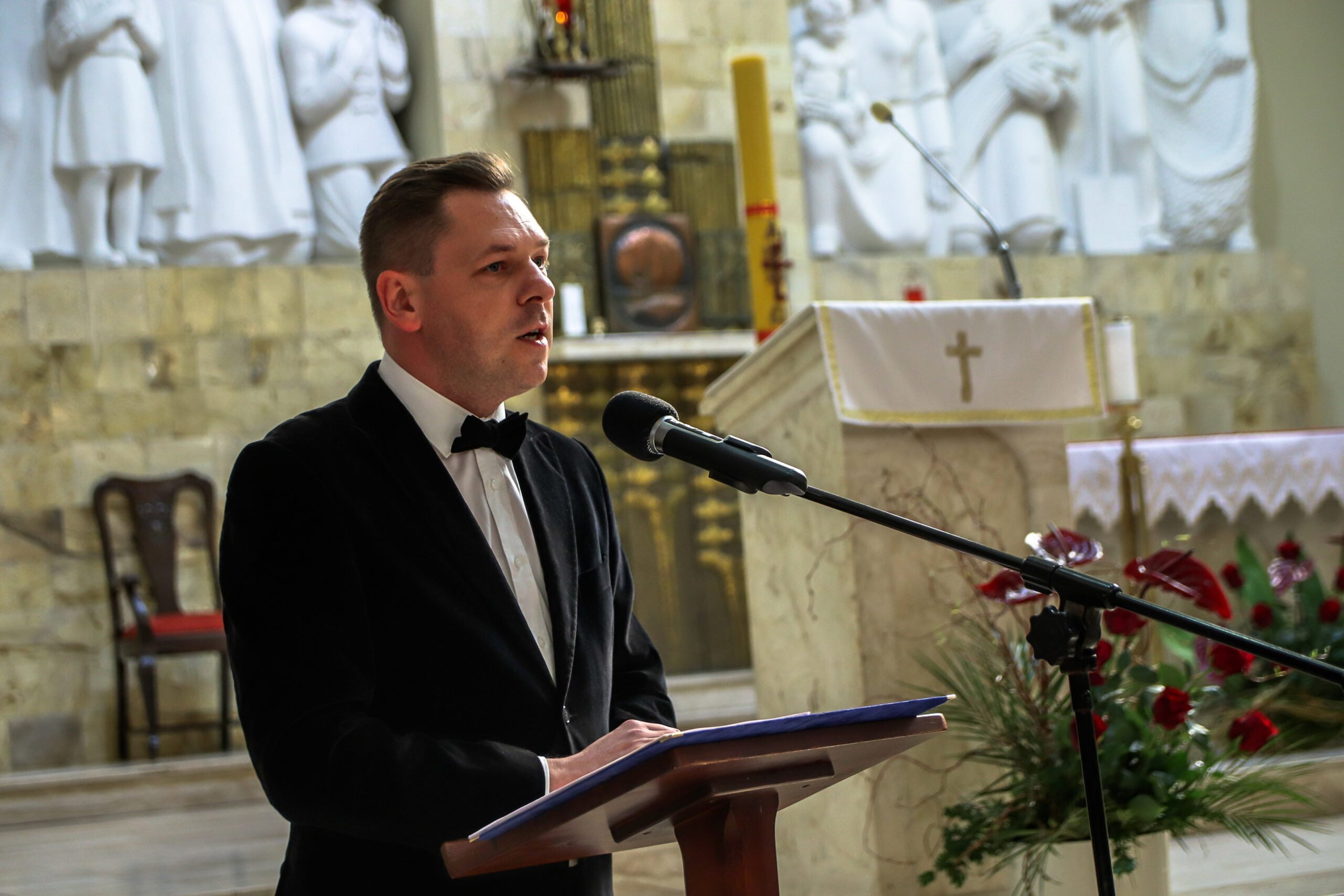 Przy mównicy na tle ołtarza stoi mężczyzna w garniturze 