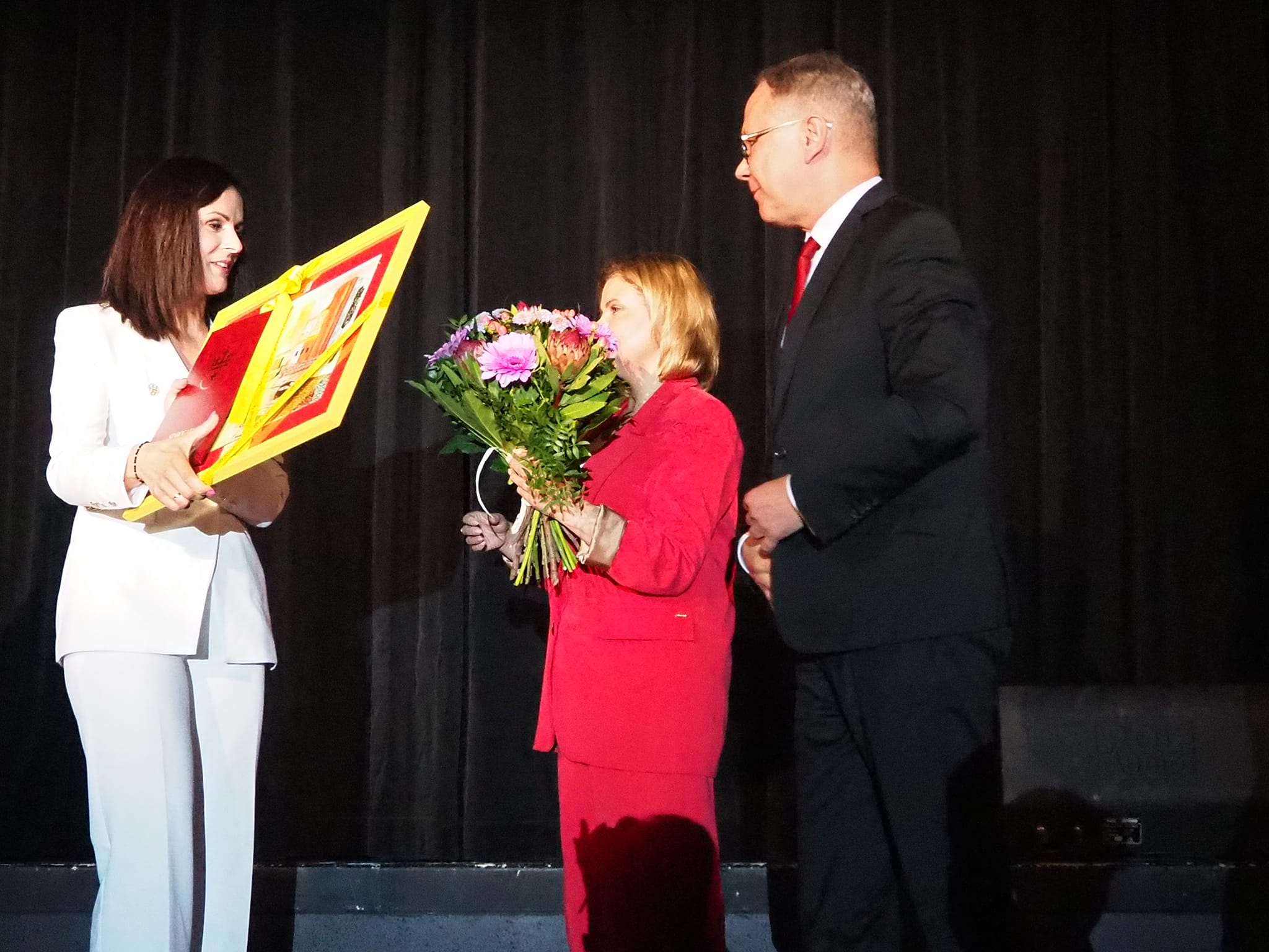 Podziękowania i życzenia na ręce dyrektora SCK Ewy Roman składają Prezydent Miasta Starogard Gdański Janusz Stankowiak i Przewodnicząca Rady Miasta Anna Benert. Trzy osoby stoją na scenie. 