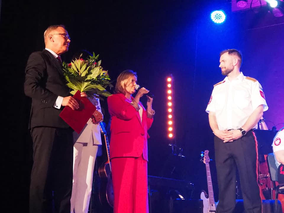 Prezydent Miasta, Przewodnicząca Rady Miasta oraz dyrektor SCK składają gratulacje dla Orkiestry na ręce dyrygenta Kacpra Roszkowskiego. Cztery osoby na scenie. 