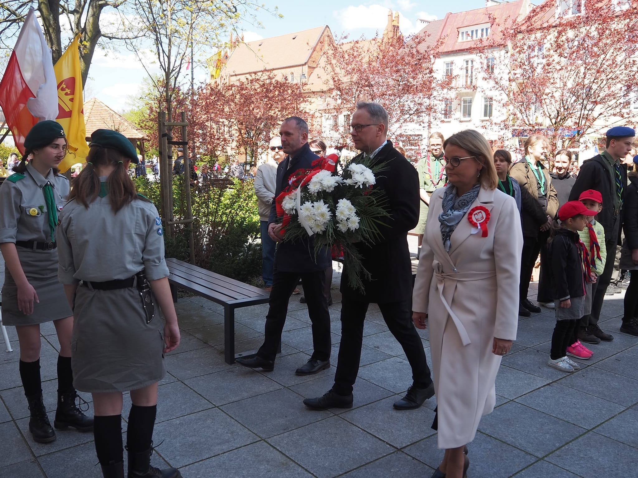 Władze miasta (od prawej): Przewodnicząca Rady Miasta Anna Benert, Prezydent Miasta Janusz Stankowiak i wiceprezydent Maciej Kalinowski składają wiązankę kwiatów pod tablicą upamiętniającą powrót Starogardu do Państwa Polskiego. Na zdjęciu więcej osób, trzy osoby na pierwszym planie. Kwiaty odbierają harcerze. 