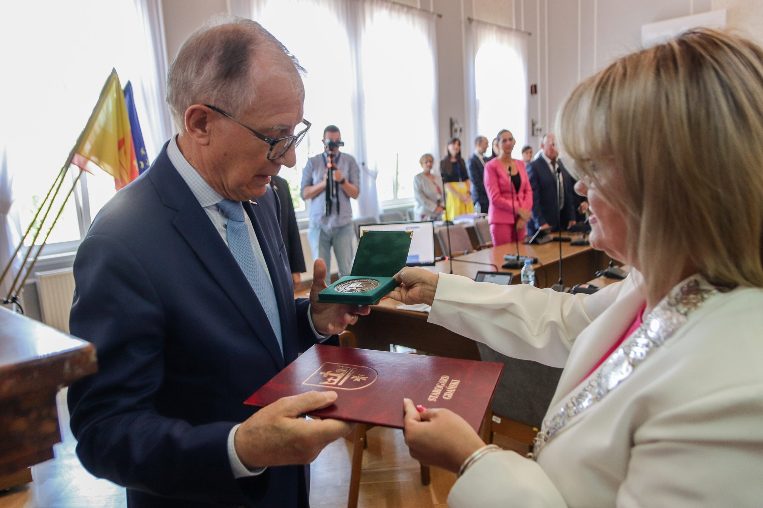 Kobieta wrecza mężczyżnie medal . W tle soją ludzie - radni