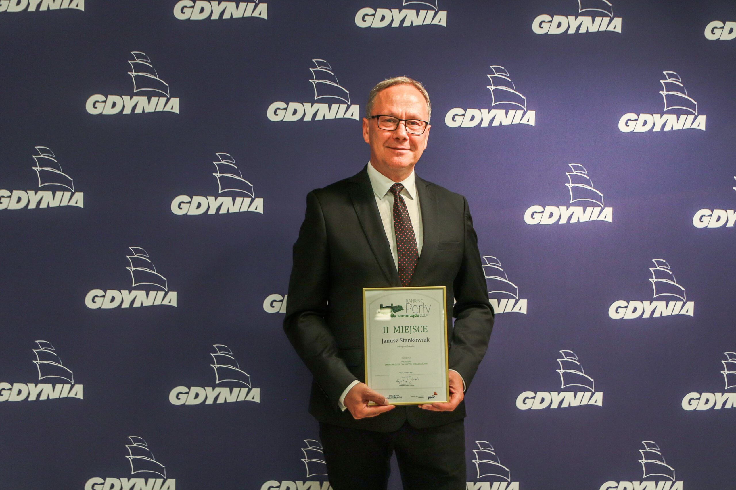 Prezydent Miasta Janusz Stankowiak z dyplomem w dłoniach stoi na tle ścianki Miasta Gdynia