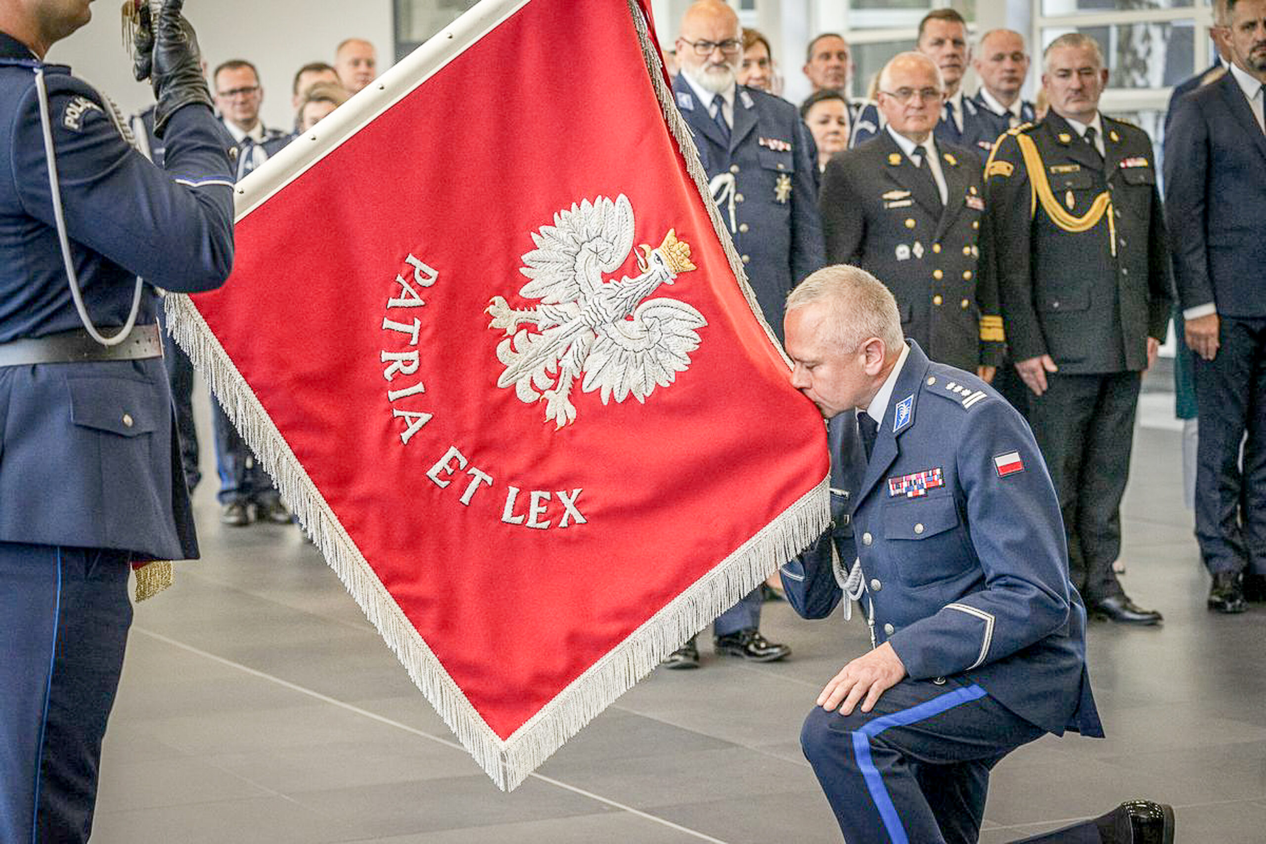 Meżczyzna kleka przed sztandarem Policji