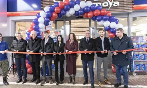 Grupa ludzi trzyma w dłoniach czerwoną wstęgę szykujac się do jej przecięcia 