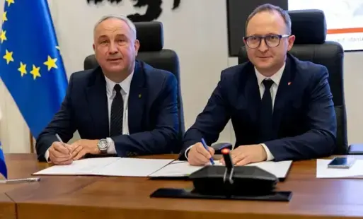 dwóch mężczyzn w garniturach siedza przy stole i podpisują dokumenty