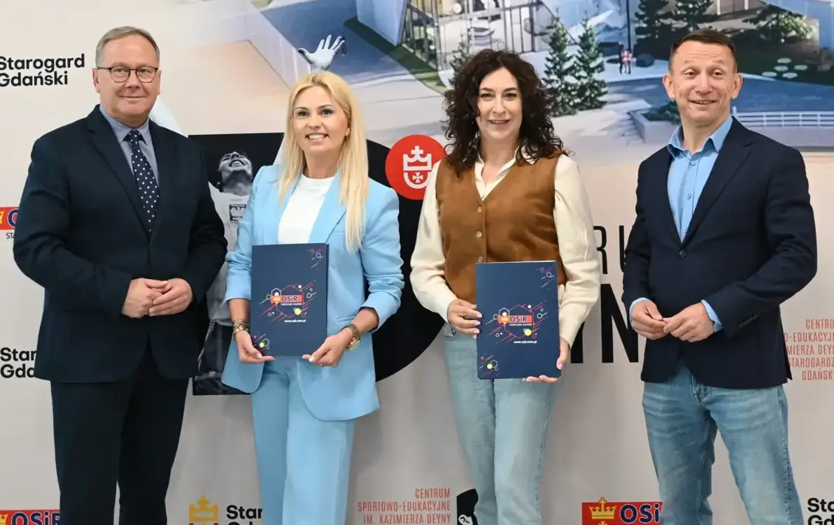 Dwóch męzczyzn w garniturach i dwie kobiety w środku elegancko ubrane trzymaja teczki z podpisanymi umowami