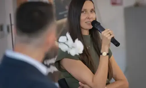 Kobieta w długich włosach z mikrofonem w reku rozmawia z mężczyznom odwróconym tyłem