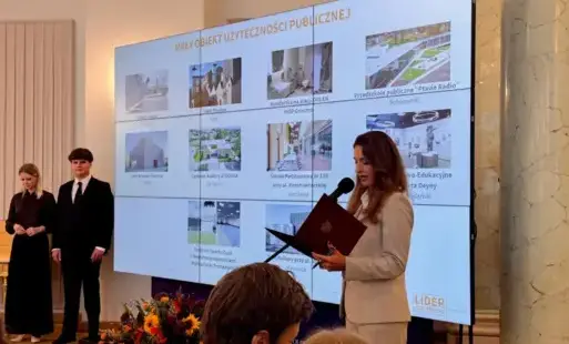 Kobieta na tle tablicy z finalistami konkursu Lider Dostępności w kategorii Mały obiekt użyteczności publicznej