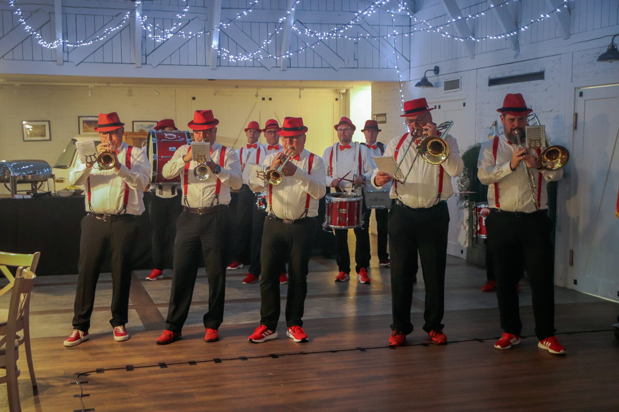 12 mężczyzn w białych koszulach czerwonych szelkach i muszkach i czarnych spodniach gra na instrumentach 